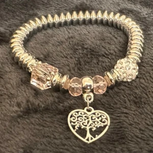 Romantiskt boho armband med rosa pärlor och hjärthänge - Elastiskt armband i silvrig metall med glittriga rosa pärlor och ett vackert hjärthänge med livets träd. Perfekt för dig som gillar en romantisk och boho-inspirerad stil. Stretchdesign gör det enkelt att ta på. Passar de flesta handleder. Innerdiameter (vilande): ca 5,5 cm.  Priset är redan lågt, så prutning accepteras ej – men jag erbjuder rabatt vid köp av flera plagg. Kika gärna på mina andra annonser också, jag rensar både garderob och smyckesskrin!  