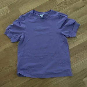Lila topp från Vero Moda  - Superfin lila topp från Vero Moda i storlek XS. T-shirten har puffiga korta ärmar och rund halsringning. Enkel och stilren design i mjuk bomull, perfekt att matcha med jeans eller kjol för en trendig look.💗❤️