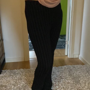 Svarta randiga bootcut byxor - Snygga svarta byxor med tunna vita ränder och bootcut-snitt. De har hög midja och sitter tajt upptill med utsvängda ben. Perfekta för dig som gillar en stilren och trendig look. Materialet känns mjukt och stretchigt, vilket gör dem riktigt bekväma.