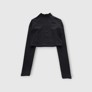 Svart croppad långärmad tröja - Svart croppad långärmad tröja med hög hals. Tröjan har en slim och stilren passform som sitter snyggt på kroppen. Perfekt att matcha med höga jeans eller kjol för en clean look. Materialet känns mjukt och stretchigt, troligtvis bomull eller polyester.