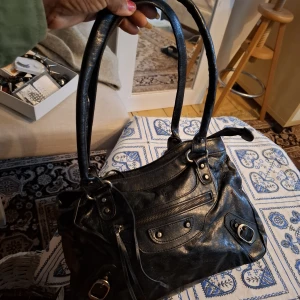 Svart handväska i skinn Accessorize - Snygg svart handväska från Accessorize i mjukt skinn med dubbla handtag, dragkedja upptill och coola metalldetaljer. Väskan har en praktisk ytterficka med dragkedja och flera fack inuti för dina grejer. Perfekt storlek för att få plats med allt du behöver.