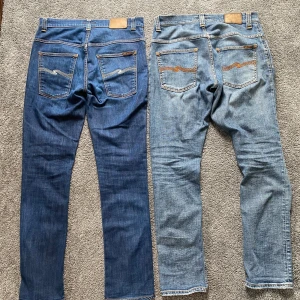 2 par Nudie Jeans, blå & ljusblå, W34/L34 & W30/L32 - Två par Nudie Jeans säljes! Ett par i mörkblå denim och ett par i ljusblå tvätt med slitningar och hål på knäna. Båda har klassiska Nudie-sömmar på bakfickorna och orange kontrastsömmar. Perfekta jeans för dig som gillar snygg och avslappnad stil.