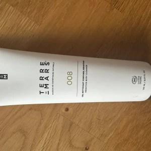 Terre de Mars body cleanser 008 - En stilren vit tub med Terre de Mars 008 body cleanser. Tuben rymmer 150 ml och har minimalistisk design med svart och guld text. Ekologiskt certifierad och perfekt för dig som gillar naturliga produkter.