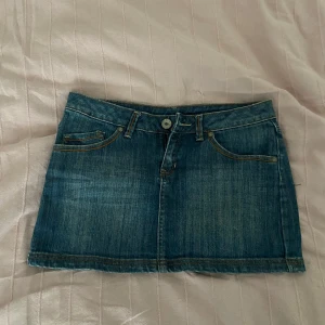 Jeanskjol med broderade bakfickor - Snygg blå jeanskjol med klassisk femficksdesign och broderade detaljer på bakfickorna. Kjolen har bälteshällor, knapp och dragkedja framtill. Perfekt för dig som gillar en avslappnad men trendig stil.