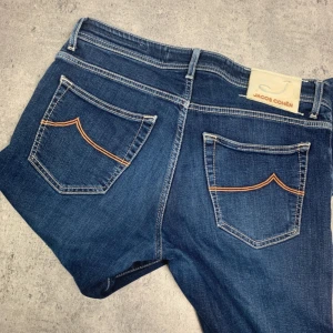 Blå jeans från Jacob Cohën, stl 34 - Snygga blå jeans från Jacob Cohën med klassisk femficksdesign och kontrastsömmar på bakfickorna. Jeansen har rak passform och är tillverkade i mjukt bomullsjeans med en hint av stretch. Perfekta för dig som gillar italiensk design och detaljer.