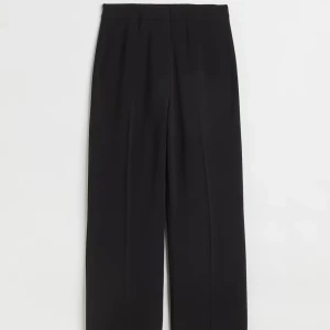 Svarta vida kostymbyxor - Stilrena svarta kostymbyxor med hög midja och vida ben. Byxorna har pressveck, dold dragkedja och hake i midjan för en clean look. Perfekta till en snygg topp eller kavaj. Materialet är mjukt och faller snyggt.