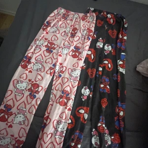 Hello Kitty x Spiderman pyjamasbyxor - Unika pyjamasbyxor med ena benet i ljusrosa med Hello Kitty och hjärtan, andra benet svart med Spiderman och Hello Kitty-motiv. Mjukt material och resår i midjan för extra komfort. Perfekt för dig som älskar coola och lekfulla prints.