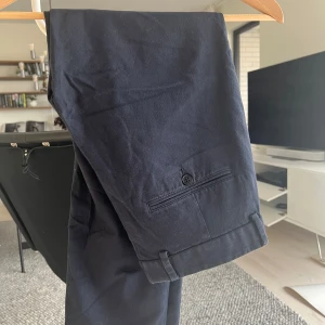 Mörkblå kostymbyxor J.Lindeberg - Snygga mörkblå kostymbyxor från J.Lindeberg i klassisk rak modell. Byxorna har bakficka med knapp och stilrena detaljer. Perfekta för en clean och dressad look. Tillverkade i bomullsmix för skön känsla.
