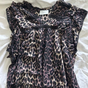 Leopardmönstrad blus från Neo Noir - Säljer en luftig blus från Neo Noir med leopardmönster i svart, beige och bruna toner. Blusen har volangdetaljer vid axlar och halsringning, v-ringad front och är ärmlös. Perfekt för dig som vill sticka ut med ett djurmönster och coola detaljer.