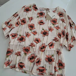 Blommig blus från Mos Mosh - Supersöt blus från Mos Mosh med stort blommönster i rosa och rött på ljus botten. Modellen har korta ärmar, rund hals och dragsko i midjan för en snygg passform. Tillverkad i mjuk viskos som känns skön mot huden. Nypris 1149 sek på Boztlet. Blusen är helt ny. 