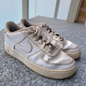 Nike Air Force 1 vita sneakers - Klassiska Nike Air Force 1 sneakers i vitt skinn. Lågt skaft, rund tå och snörning framtill. Perforerade detaljer på tån för extra ventilation. Perfekt för dig som gillar en tidlös streetstil. Slitna men har lite kvar att ge 🙂