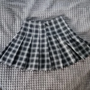 Kjol i svartvitt rutmönster, storlek 32 - Snygg svart kjol från H&M, storlek 32. Bara använd en gång – i nyskick utan några defekter! Materialet är mjukt och följsamt, vilket gör den bekväm att bära hela dagen.