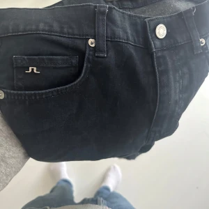 Svarta jeansbyxor från J.Lindeberg - Snygga svarta jeansbyxor från J.Lindeberg med klassisk femficksdesign och silverfärgade detaljer. Byxorna har rak passform och är tillverkade i ett mjukt jeanstyg som sitter skönt hela dagen. Perfekta för dig som gillar stilrena och tidlösa plagg.