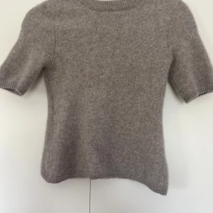 Grå kashmirtröja XS - Supermjuk och fluffig grå/beige kashmir t-shirt från H&M premium i storlek XS. Tröjan har korta ärmar, rund halsringning och ribbade muddar. Nypris är 990 kronor