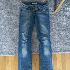 Blå bootcut jeans från Vero Moda - Snygga blå jeans från Vero Moda med bootcut passform och slitna detaljer på benen. Jeansen har klassisk femficksdesign, dragkedja och knapp framtill samt coola slitningar och tvättade partier för en trendig look.