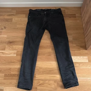 Svarta Replay Anbass Hyperflex jeans - Svarta Replay Anbass Hyperflex jeans med smal passform och klassisk femficksdesign. Jeansen är tillverkade i stretchigt denim för extra komfort och har diskreta slitningar för en cool look. Perfekta för dig som gillar stilrena och bekväma jeans. 