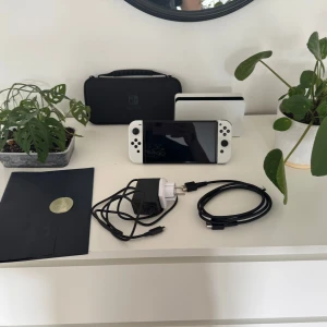 Nintendo switch oled from Japan with recite + collective object+many more things - INCLUDED🥰:  -Konsol skydd (rosa, silikon ’cinnamonroll’).  -Väska med spelfack inuti -speldosa x1 -laddare -texturerat samlingskort på ’tears of the lost kingdom’  -Har skärmskydd på -Joycons straps  SÄLJER: Säljer en Switch Oled från Nintendo i färgen vit. Produkten är köpt i Japan (kvitto finns i det blå kuvertet) under en promotion collection och kom därför tillsammans med ett samlingskort för Zelda spelet (Tears of the lost Kingdom) i kuvert av begränsat antal.  SKICK: Som ny,sparsamt använd