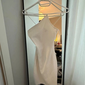 Vit ribbad asymmetrisk klänning - Säljer en vit, ribbad kortklänning med asymmetrisk design och tunna axelband. Klänningen är figurnära och har en modern, stilren look som passar perfekt för dig som gillar trendiga plagg med unik form. Stretchig 