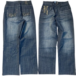 Karl Kani blå baggy jeans med brodyr - Blå jeans från Karl Kani med bred passform och stora broderade loggor på fickorna och framtill. Snygga detaljer med nitar och kontrastsömmar. Klassisk femficksmodell i denim med streetkänsla.