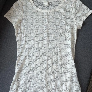 Vit spetsblus med blommönster - Säljer en söt vit blus från H&M i genombruten spets med blommigt mönster. Modellen är figurnära med korta ärmar och rund halsringning.