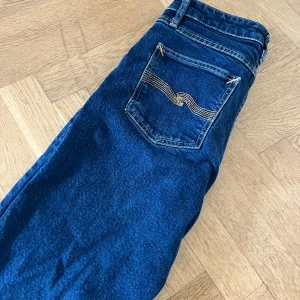 Mörkblå slim fit jeans från Nudie Jeans - Säljer ett par mörkblå slim fit jeans från Nudie Jeans med klassiska kontrastsömmar och broderad bakficka. Hör av vid funderingar och pris!