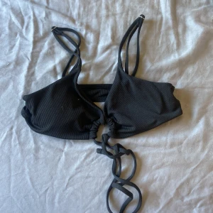 Svart ribbad bikiniöverdel XS - Snygg svart bikiniöverdel i ribbat material med dubbla smala axelband och trendig snörning framtill. Perfekt för stranden eller poolen, modellen har en cool och modern look med justerbara band för bästa passform.