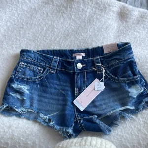 Extra low denim shorts Gina tricot  - Snygga blå jeansshorts från Gina Tricot nya kollektion, med låg midja, slitna detaljer och fransig kant. Klassisk femficksmodell med coola sömmar bak och bälteshällor. Säljer därav de inte satt så som jag önskat på mig, HELT NYA MED PRISLAPP PÅ!💗