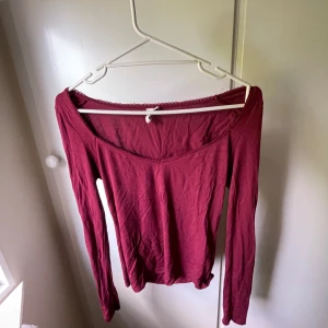 Vinröd långärmad topp med spetskant - Vinröd långärmad topp från Nelly i storlek M. Toppens halsringning är dekorerad med en söt spetskant och har en lätt utdragen u-ringnig. Materialet är tunt och mjukt, perfekt för lager-på-lager eller nu i sommarens värme. Enkel och stilren design som passar till många outfits.