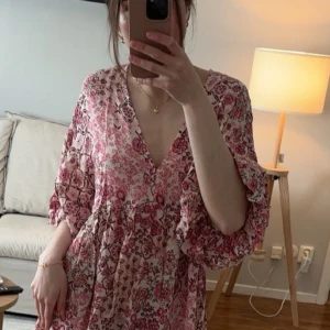 Blommig kortklänning från Zara XS - Intressekoll på supersöt kortklänning från Zara i ljusrosa med vinröda toner med blommigt mönster. Klänningen har v-ringning, korta vida ärmar och ett luftigt fall.  Storlek xs. Helt ny