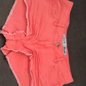 Korallrosa jeansshorts med fransar - Snygga korallrosa jeansshorts från Denim Co med råa fransade kanter och klassisk femficksmodell. Shortsen har hög midja och är perfekta för varma dagar. Stängs med knapp och dragkedja framtill. Superfina till sneakers eller sandaler!