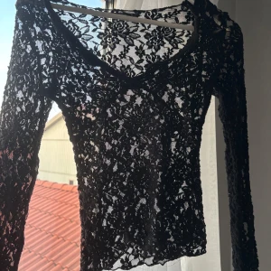 Svart spetsblus från Gina Tricot XS - Supersnygg svart långärmad blus i spets från Gina Tricot. Blusen har v-ringning och är helt genombruten med blommigt spetsmönster. Perfekt för dig som vill sticka ut med en feminin och trendig look. Säljer pga att den tyvärr har blivit för liten. Kan vara så att tröjan är lite sliten vid vissa områden men inget som tänks på.