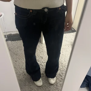 Mörkblå bootcut jeans från True Religion - Säljer ett par mörkblå jeans från True Religion med bootcut passform. Jeansen har klassiska kontrastsömmar, fem fickor och snygga detaljer på bakfickorna med knapp. Perfekta för dig som gillar en tidlös och trendig look.