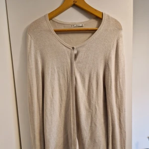 Beige kofta från Zara Knit med knappar - Beige kofta från Zara Knit i mjukt stickat material. Rund halsringning och långa ärmar med snygga silverfärgade knappar längs ärmsluten.