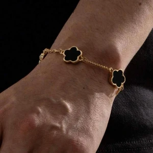 Guldarmband med svarta blommor - Snyggt armband i guldton med svarta blommor som detaljer. Kedjan är tunn och smidig, och blommorna har en stilren, rundad form. Perfekt accessoar för att lyfta din outfit med en elegant touch.