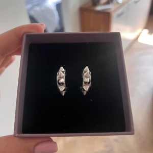 Silvriga örhängen med nitar - Coola silvriga hoops med markerade nitar runt hela örhänget. De har en chunky känsla och ger en edgy vibe till din stil. Perfekta för dig som gillar att sticka ut och vill ha något unikt i smyckeskrinet.