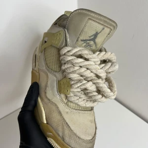 Nike Air Jordan 4 Off-White Sail custom made  - Exklusiva Nike Air Jordan 4 Off-White Sail med chunky rep-liknande snören och ikoniska detaljer som genomskinliga paneler och 'AIR'-text på sulan. Skorna har en beige och ljusgul färgskala, mesh och skinnmaterial samt klassisk Jordan-logga på plösen.
