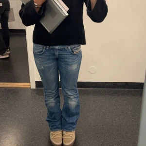 Blå bootcut jeans med slitningar diesel  - Säljer ett par snygga blå bootcut jeans från diesel med lätt slitna detaljer och klassisk femficksdesign. Jeansen har låg midja och en cool tvätt som ger en avslappnad vibe. Perfekta till sneakers eller boots.