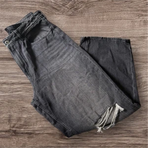 Gråa wide jeans med slitna knän - Snygga grå jeans med bred passform och slitna detaljer över båda knäna. Jeansen har klassisk femficksdesign, bälteshällor och dragkedjegylf och är höga i midjan. Perfekta för en avslappnad och trendig look.