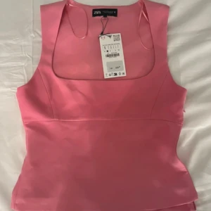 Rosa linnetopp från Zara - Supersnygg rosa linnetopp från Zara med fyrkantig urringning och breda axelband. Toppen har en figurnära passform och är gjord i ett slätt, lätt glansigt material som känns lyxigt. Perfekt att styla med jeans eller kjol för en trendig look.