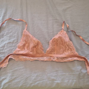 Rosa spets bralette från H&M - Supersöt rosa bralette från H&M med tunna axelband och vackra spetsdetaljer. Triangelkupor och bred spetskant nedtill ger en romantisk vibe. Perfekt att styla under en öppen skjorta eller som den är till höga jeans.