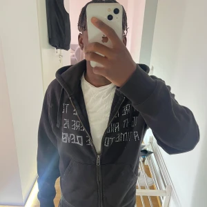 Svart hoodie med text och dragkedja - Svart hoodie med huva och dragkedja framtill. På bröstet står texten 'There is a time to fight and there is a time to be clever' i vita prickar. Tröjan har känguruficka och snörning i huvan. Perfekt för en chill och avslappnad stil.