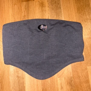 Grå randig halsvärmare Champion - Snygg grå halsvärmare från Champion med diskreta ränder och broderad logga framtill. Perfekt för kalla dagar när du vill hålla stilen och värmen. Mjuk och stretchig passform som sitter skönt runt halsen.