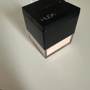 Huda Beauty Peach Pie Baking Powder - Lös baking & setting powder i nyansen Peach Pie från Huda Beauty. Kommer i en fyrkantig burk med svart lock och transparent botten. Perfekt för att sätta sminket under ögonen, T-zonen och haka. Ger en matt finish och jämnar ut hudtonen. Använd fåtal gånger
