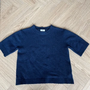 Mörkblå stickad tröja Kappahl - Enkel och stilren mörkblå stickad tröja från Kappahl med korta ärmar och ribbade muddar vid hals, ärmslut och nederkant. Perfekt för lager-på-lager och funkar året runt. Snygg till både jeans och kjol.