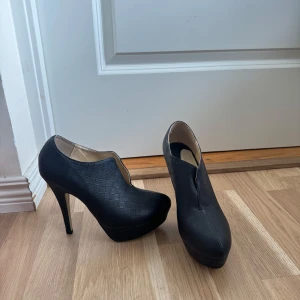 Svarta stövletter med hög klack - Snygga svarta stövletter med hög klack och plattform. Skorna har ett diskret rutmönster i materialet och en elegant, rund tå.
