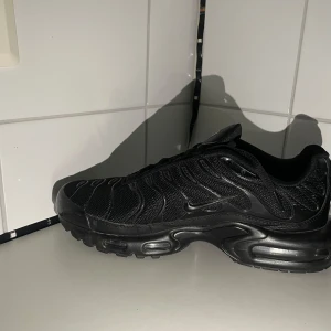 Nike Air Max Plus helsvarta sneakers - Den hära skorna är helt ny och o använt Nike Air Max Plus i helsvart med mesh och syntetpaneler, ikoniska vågformade detaljer och Tn Air-logga på hälen. Skorna har synlig Air-dämpning i sulan och snörning för perfekt passform. Perfekta för dig som gillar streetwear och sportig stil.