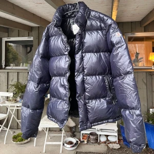 Mörkblå Moncler pufferjacka - Säljer en svart pufferjacka från Moncler med klassisk logga på armen och dragkedja och två fickor med dragkedja. Står size 5 i Moncler stlk men verkar mer som en L 