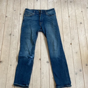 Blå jeans från Jack & Jones, 29/30 - Snygga blå jeans från Jack & Jones i klassisk modell med raka ben och fem fickor. Jeansen har kontrastsömmar och en mörk tvätt med lätt slitning. Tillverkade i bomull för en skön känsla och stilren look.