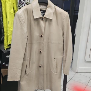 Beige skinnrock från Petroff, stl 42 - Stilren beige vintage skinnrock från Petroff i äkta läder. Klassisk rak modell med krage, knäppning med fyra knappar och två fickor framtill. Perfekt för dig som gillar minimalistisk och tidlös stil. Passar lika bra till jeans som till dressade byxor. Små defekt vid båda fickor. 