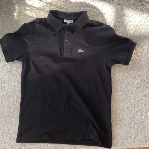 Svart pikétröja från Lacoste - Klassisk svart pikétröja från Lacoste. Har inte använt den en endaste gång. Bästa skicket! Allt jag fick när köpte den ingår! Nypris 900kr. Priset kan diskuteras!🧩